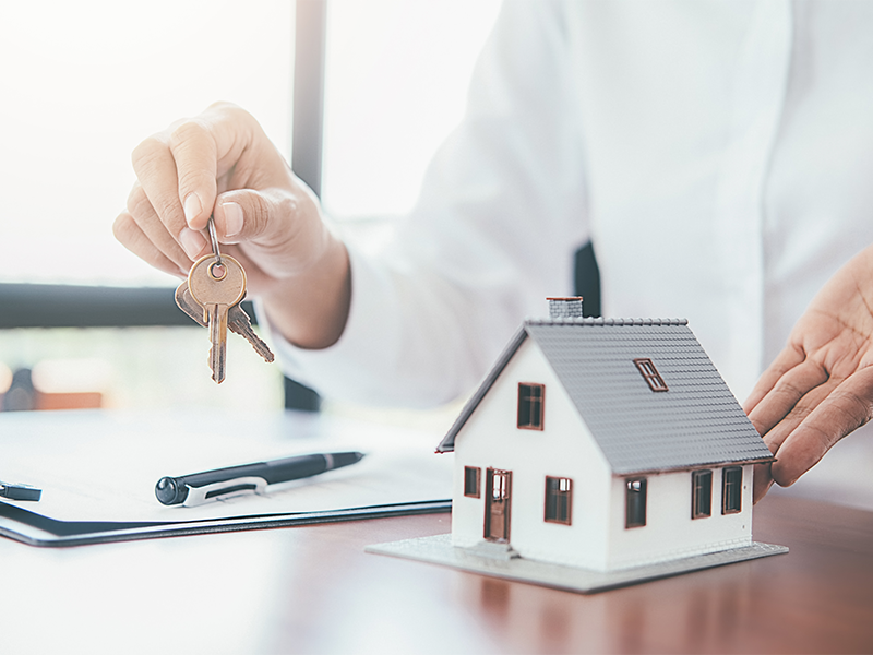 A person hold house keys besides a small model home